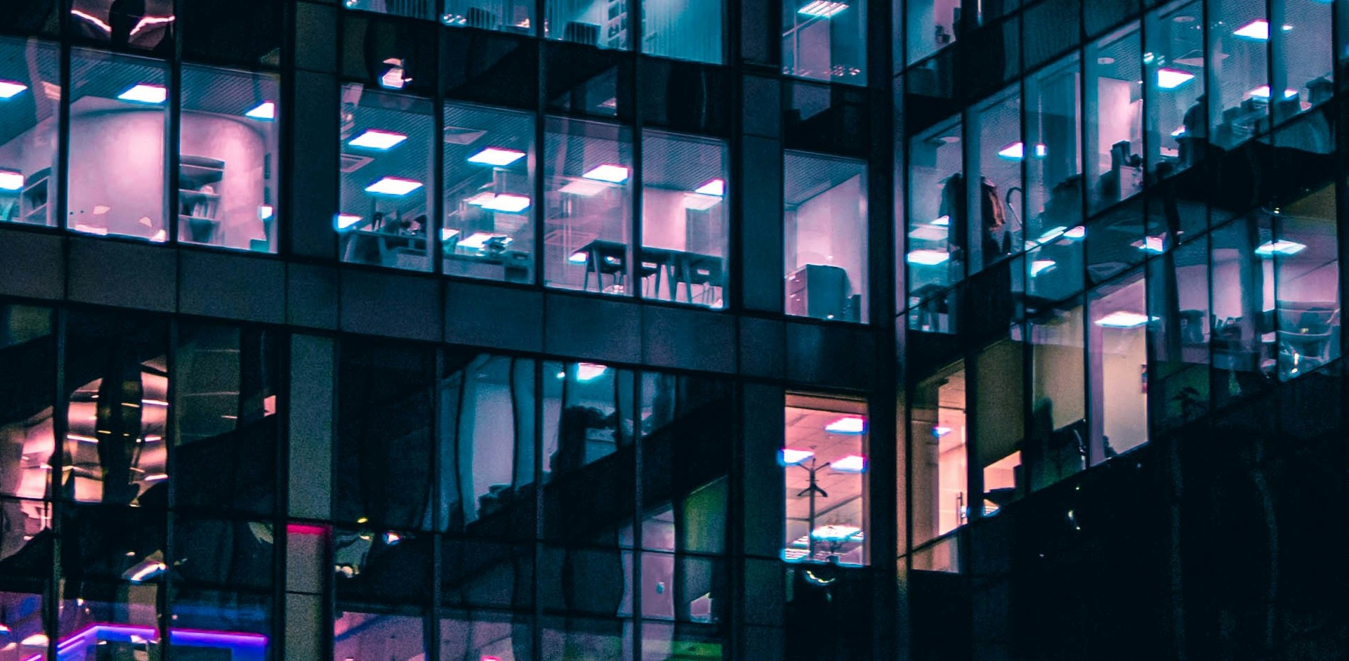 Night view of a lit office building through glass windows.