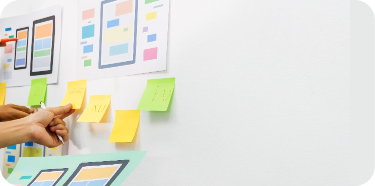 A board with a lot of paste-it notes on it. A hand is pointing to one of the notes. Denotes the UX design process.