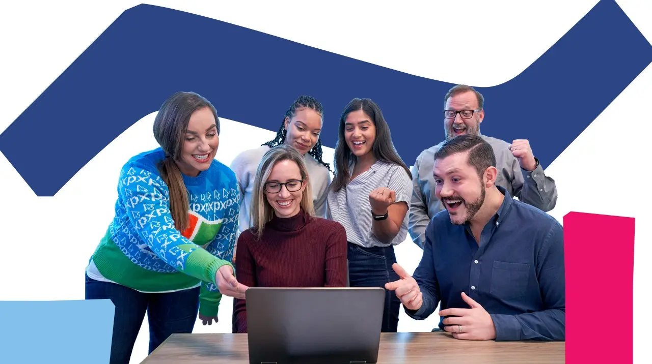 A group of colleagues are gathered around a laptop. All of them are laughing or similing at something being displayed on the laptop.